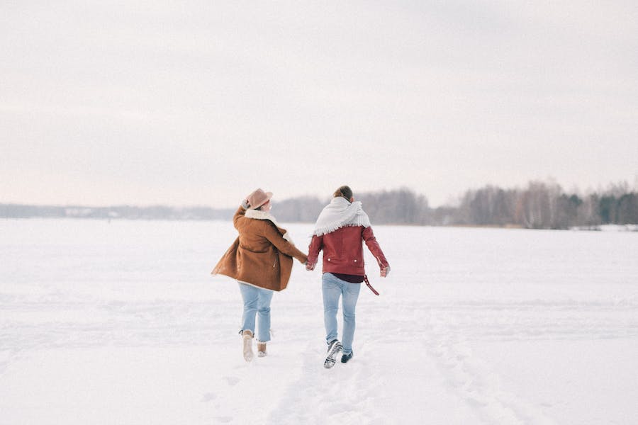 Momak i devojka šetaju po snegu držeći se za ruke