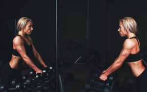 Žena se gleda u ogledalo dok drži tegove.