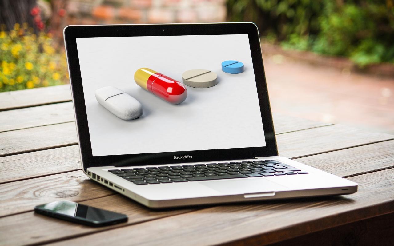 Pilule i tablete na ekranu laptopa koji je na drvenom stolu