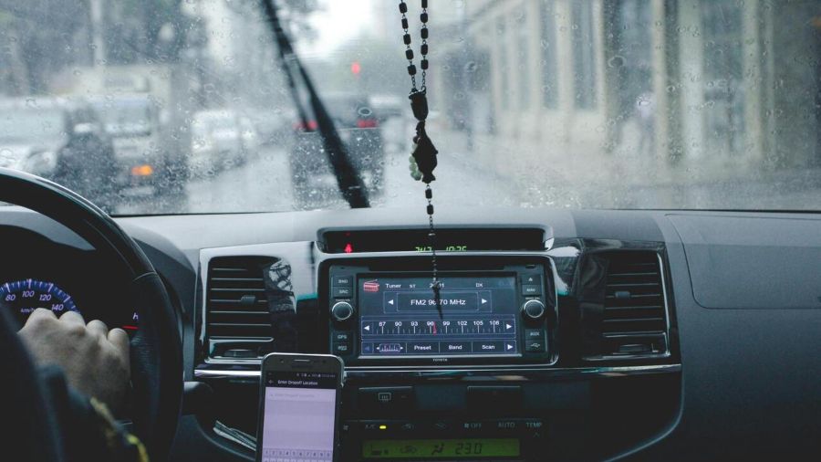 Pogled iz unutrašnjosti automobila kroz mokar vetrobran na volan, kontrolnu tablu i mobilni