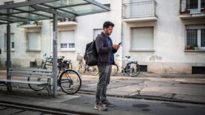 Muškarac sa ruksakom stoji na tramvajskoj stanici i gleda u telefon