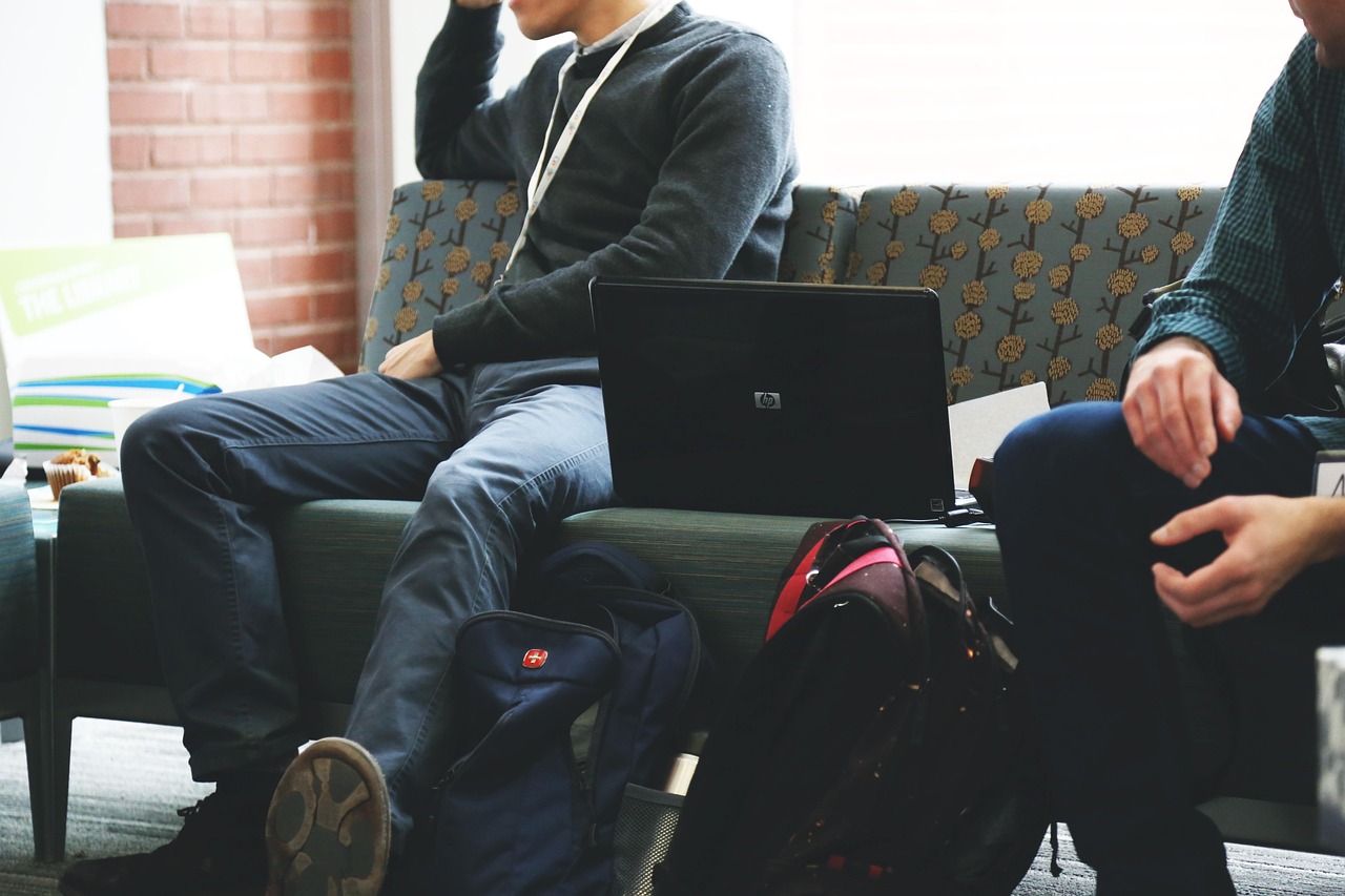 Momci sede na dvosedu dok jedan od njih radi na laptopu
